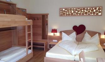 A cozy room with wooden furniture and a double bed. There is a bunk bed and pleasant lighting from table lamps.