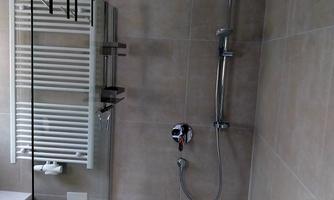 A modern shower with a glass partition and an elegant rain shower. The walls are kept in neutral, light tones.