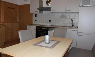 A modern kitchen with a dining table and chairs. The equipment includes a stove, a microwave, and wooden cabinets.