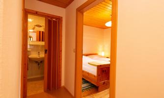 A bright corridor with two doors. On the left side, there is a bathroom and on the right side, a bedroom with a cozy bed.