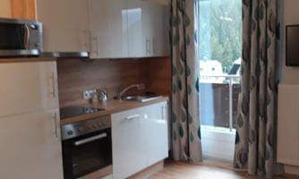 A modern kitchen with white cabinets and wood details. The window offers a view of a balcony and the surrounding nature.