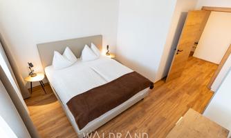 A modern bedroom with a comfortable double bed and bright wooden floors. On the sides are nightstands with lamps.
