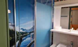 A modern bathroom with a shower cabin decorated with a beautiful mountain lake motif. The room has bright colors and is well-lit.