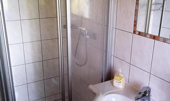 A bathroom with a shower and a sink. The walls are tiled and light.
