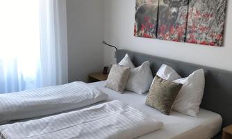A cozy bedroom with a double bed and pillows. On the wall hangs a picture of a decorative forest motif.