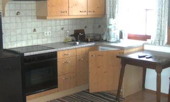 A modern kitchen with wooden cabinets and a stove. A table is by the window with a view of nature.