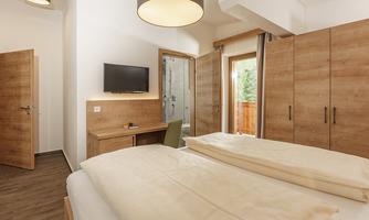 A modern bedroom with wood decor and a cozy atmosphere. It features a double bed, a desk, and a small balcony.
