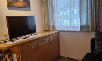 A cozy living area with a television and a sideboard. A large window with curtains lets in plenty of light.