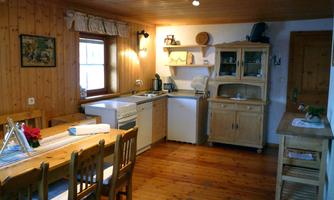 A cozy kitchen with wood paneling and a dining table. There are modern appliances and plenty of natural light.