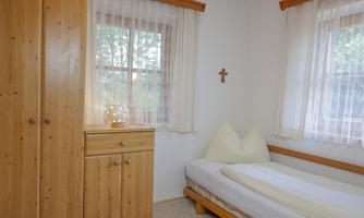 A simple bedroom with a bed, a wooden wardrobe, and bright curtains. The room feels bright and inviting.