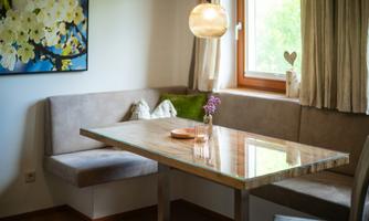 A cozy dining area with a modern wooden tabletop and a beige bench. The window lets in plenty of natural light.
