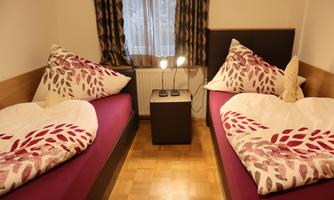 A cozy bedroom with two single beds and colorful cushions. Next to the beds is a nightstand with two lamps.