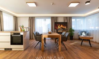 A modern living kitchen with wooden floors and large windows.  
The dining area is cozy, furnished with a wooden table and chairs.