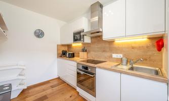 A modern kitchen with white furniture and light wood. It is well-equipped and offers a warm atmosphere.