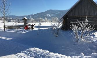 A snowy landscape with a wooden house and snow-covered trees. The sun is shining clearly in the blue sky.