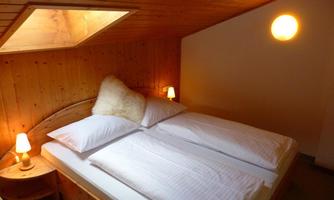A cozy bedroom with a double bed and wooden paneled walls. Soft lighting creates a relaxed atmosphere.