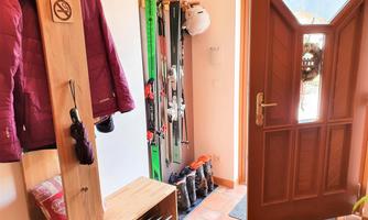 A cozy entrance area with a wooden bench, where ski equipment and jackets are hung. The door is open, letting in daylight.