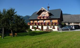 A charming house with flowered balconies in a green landscape. In the background, mountains and a blue sky are visible.