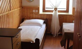 A simple room with wood paneling and two beds. A window with a white curtain provides daylight.