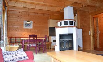 A cozy living area with wooden paneling and a fireplace. There is a dining area with a table and chairs as well as a red couch.