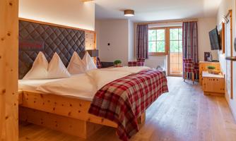 A cozy hotel room with a large bed and wooden details.  
Large windows let in plenty of light and offer a view of nature.