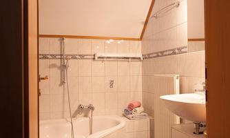 A modern bathroom with a bathtub and a sink. The walls are tiled and there are colored towels ready.