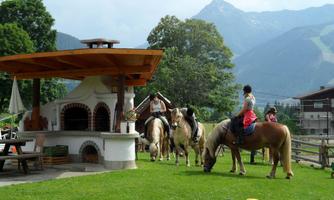 A picturesque landscape with a barbecue area and riding individuals. In the background, mountains and a lot of green meadow can be seen.