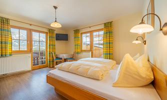 A cozy hotel room with two beds and wooden paneling. Large windows with colorful curtains provide plenty of light and a pleasant atmosphere.