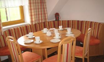 A cozy dining area with a round wooden table and upholstered seating. Coffee cups and dishes are on the table, ready for a meal.