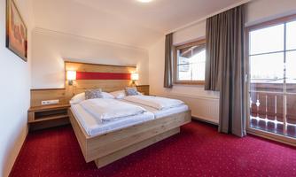 A cozy bedroom with a double bed and modern wooden design. The room has large windows and light curtains.