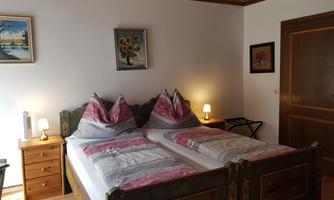 A cozy room with a double bed and traditional decorative pillows. Next to the bed are bedside lamps and a small table.