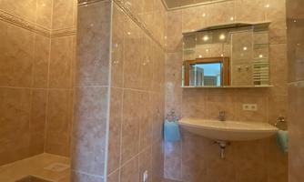 A modern bathroom with bright tiles and a large shower. The room features an elegant mirror wall and pleasant lighting.
