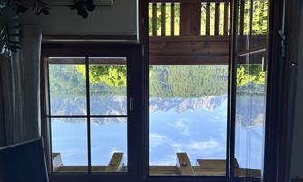 A beautiful view from a window of the mountains and the forest. The sky is clear and blue.