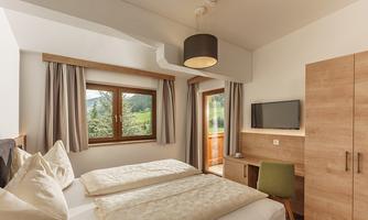 A cozy hotel room with two beds and modern wooden design. There are windows with views of nature and a small workspace.