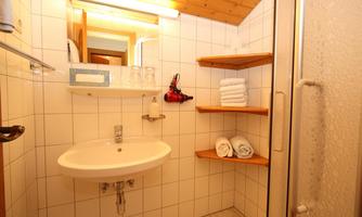 A modern bathroom with white tiles and a shower. Shelves with clean towels and glasses are available.