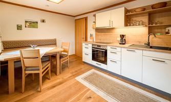 A modern kitchen with a wooden floor and bright furniture. There is a dining table with chairs and a well-equipped cooking area.