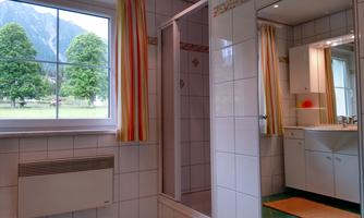 A bright bathroom with a shower and a large window. In the background, green trees and mountains can be seen.