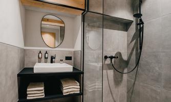 A modern bathroom with a clear glass shower and an elegant sink. The gray tiles and wood details create a stylish atmosphere.