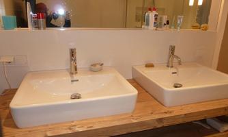 Two modern sinks on a wooden shelf in a bathroom. The mirror reflects a bright, inviting atmosphere.