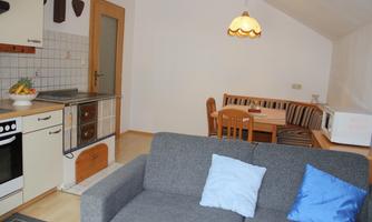 A cozy living space with a gray sofa and a dining area. The kitchen is modern and well-equipped.