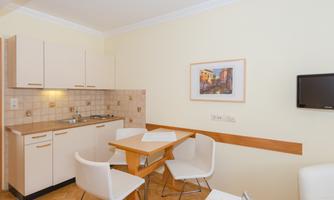 A bright kitchen with modern furniture and a table for four people. A picture hangs on the wall and a TV is mounted.