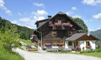 A charming wooden house with colorful flowers on the balconies. Surrounded by green forests and a clear blue sky.