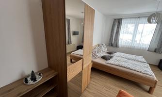 A modern bedroom with a wooden bed and a large mirror dresser. Bright walls and a window provide plenty of daylight.