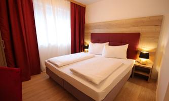 A cozy bedroom with a double bed and large windows. Red curtains and soft lighting create an inviting atmosphere.