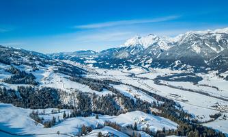 A picturesque winter landscape with snow-covered hills and mountains. The clear blue sky creates a serene atmosphere.