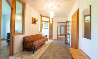 A bright hallway with wood details and a cozy sofa. A picture hangs on the wall, and there is a small shelf stand.