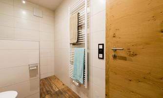 A modern bathroom with bright walls and a wooden floor. Towels hang on a radiator, and a wooden door leads outside.