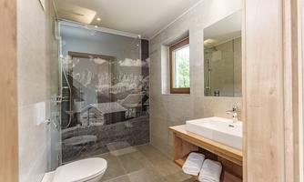A modern bathroom with a transparent shower and a large mirror. The walls are in neutral colors, and wooden accents add warmth to the space.