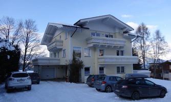 A modern house in a snow-covered environment. Several cars are parked in front of the building.