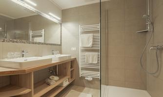 A modern bathroom with two sinks and a spacious shower. The walls are in neutral colors, and there are towels on a radiator.